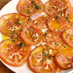 Delicioso carpaccio de tomate con aceite de oliva, ajo picado, hierbas frescas y trocitos de pistacho.