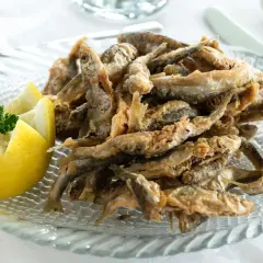 Deliciosa fritura de pescado crujiente servida en un plato con forma de pez, acompañada de limón tallado y perejil fresco.