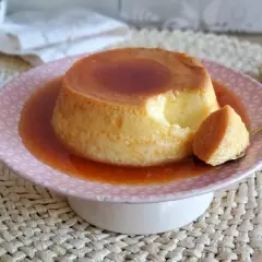 Un delicioso flan de leche condensada, con una porción servida en cuchara dorada, bañado en caramelo líquido.