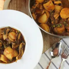 Plato de papas con choco y guisantes en salsa, servido en un cuenco blanco. Al lado, una sartén con el mismo guiso.