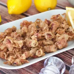 Crujientes puntillas de calamar fritas, servidas en plato blanco con limón y aceite de oliva.