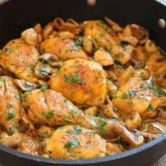 Pollo a la cerveza jugoso y dorado, con champiñones y perejil fresco, servido en una sartén.