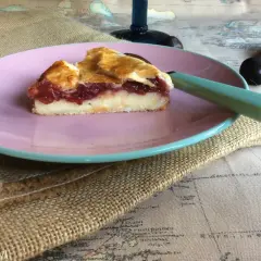 Rebanada de pastel vasco con relleno de crema y mermelada de frutos rojos, servida en plato rosa.
