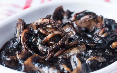 Un plato de calamares en su tinta, con tentáculos visibles y una salsa oscura y brillante.