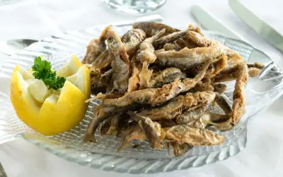 Deliciosa fritura de pescado crujiente servida en un plato con forma de pez, acompañada de limón tallado y perejil fresco.