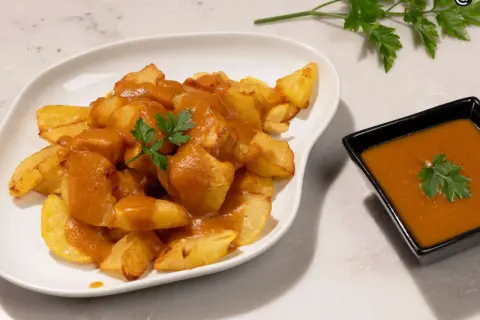 Patatas bravas crujientes cubiertas con salsa picante y perejil fresco. Un plato español delicioso.