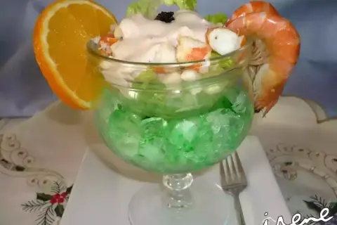 Delicioso coctel de marisco servido en copa con hielo verde, adornado con naranja y gamba.