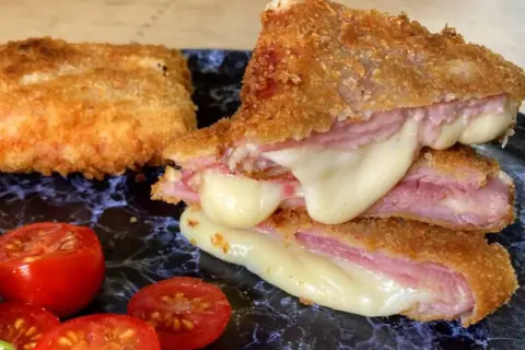 San Jacobo crujiente con queso fundido y jamón, acompañado de tomates cherry.