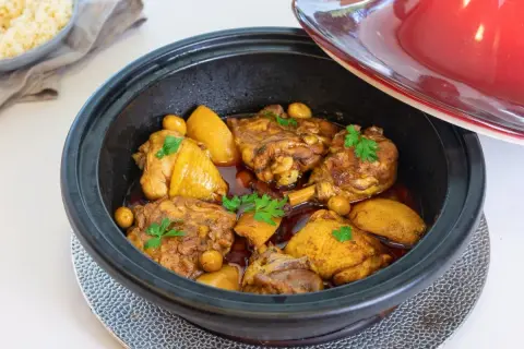 Tajín de pollo con patatas y aceitunas, decorado con perejil fresco. Un plato aromático listo para servir.