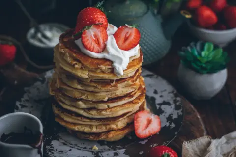 Pila de tortitas esponjosas cubiertas con nata y fresas. Una deliciosa receta de tortitas para el desayuno.