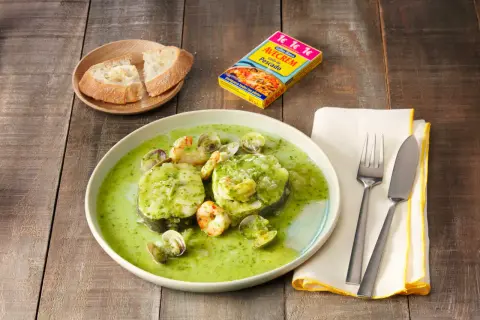 Merluza a la vasca con gambas y almejas en salsa verde, acompañada de pan.
