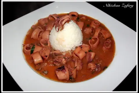 Calamares encebollados en una salsa rojiza, servidos con una bola de arroz blanco en un plato blanco.