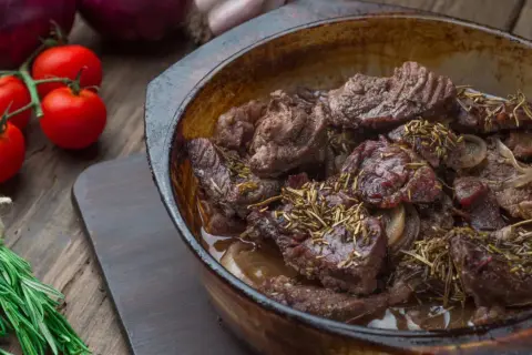 Carrilleras de ternera estofadas con romero y cebolla, servidas en cazuela de barro.