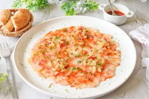 Delicioso carpaccio de gambas con aderezo y hierbas frescas, servido con panecillos.