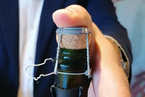 Dedo presionando el corcho de una botella de cava "CASTELL D'OR". Aprende como abrir una botella de vino espumoso.