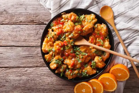 Delicioso pollo a la naranja, crujiente y bañado en una salsa dulce y cítrica, adornado con cebollín fresco.