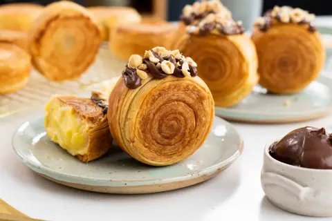 Deliciosos new york rolls cubiertos de chocolate y avellanas, uno abierto revela un cremoso relleno.