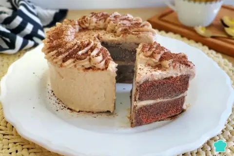 Deliciosa tarta de moka con crema y cacao espolvoreado. Un trozo cortado revela sus capas de bizcocho y relleno.
