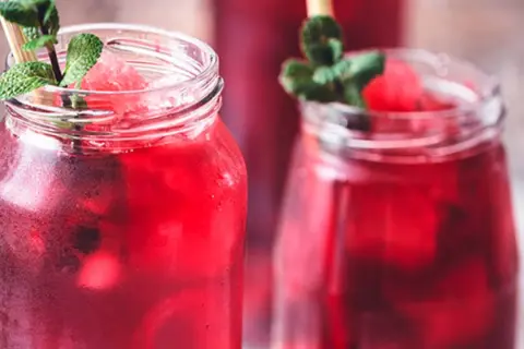 Refrescante agua de jamaica con hielo, menta y trozos de sandía en vasos rústicos.