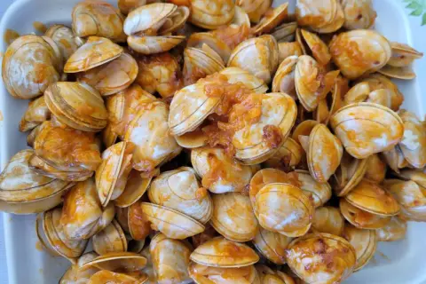 Un plato rebosante de almejas a la marinera, con su salsa anaranjada cubriendo las conchas.