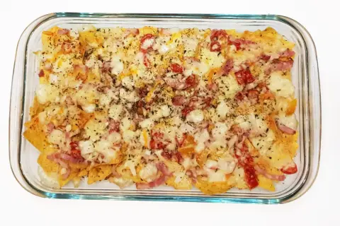 Nachos con queso recién horneados, cubiertos con trozos de tocino y pimientos rojos.