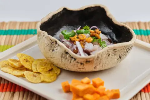 Delicioso ceviche de corvina fresco, servido en un cuenco rústico con patacones y cubos de camote.