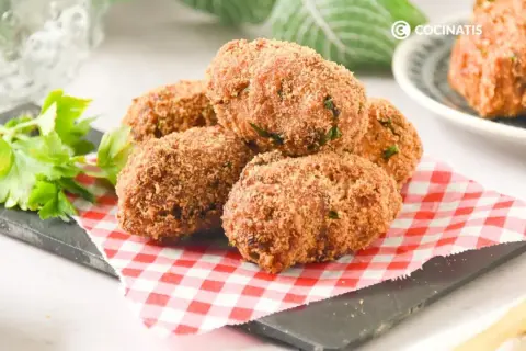 Deliciosas croquetas de atún doradas y crujientes, servidas sobre un mantel de cuadros rojos y blancos.