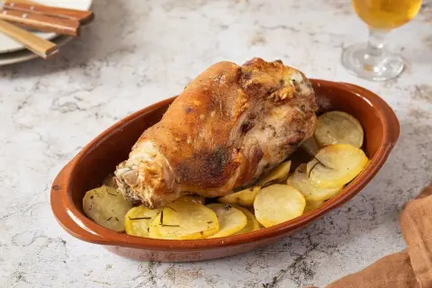 Codillo de cerdo asado, crujiente y dorado, servido en cazuela de barro con patatas panadera.