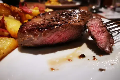 Un jugoso entrecot de ternera a la parrilla, servido con patatas doradas y un tenedor listo para degustar.