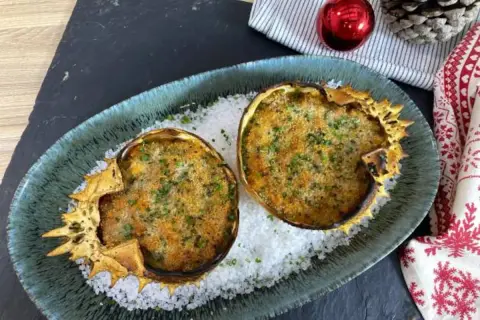 Dos deliciosos txangurros a la donostiarra, gratinados y espolvoreados con perejil, reposan sobre sal gruesa en un plato festivo.