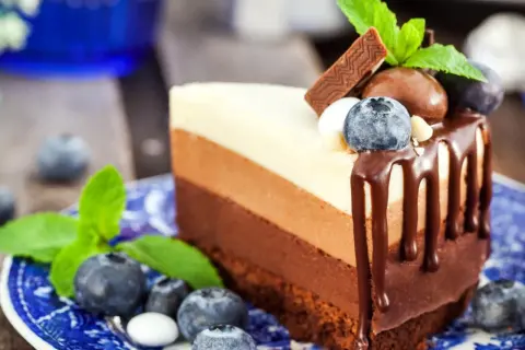 Deliciosa tarta tres chocolates en un plato azul, decorada con arándanos y menta.