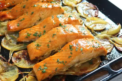 Filetes de salmón al horno, dorados y jugosos, servidos sobre patatas y cebolla asadas. Un plato delicioso y saludable.