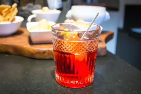 Cóctel rojo vibrante, una mezcla de vermut rojo y blanco, con guarnición de limón.