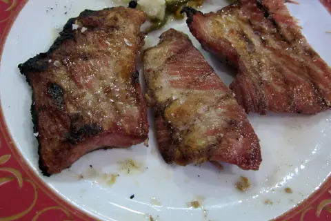 Tres jugosas porciones de secreto ibérico a la parrilla, con sal gruesa y un toque de pimienta, servidas en un plato blanco con borde decorado.