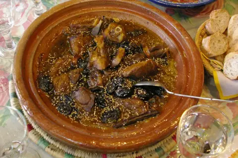Un delicioso tajine de cordero con ciruelas pasas y semillas de sésamo, servido en una cazuela de barro.