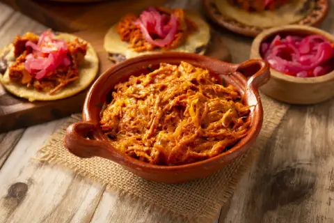 Cochinita pibil en cazuela de barro, lista para servir en tortillas con cebolla morada encurtida. ¡Un festín de sabor!