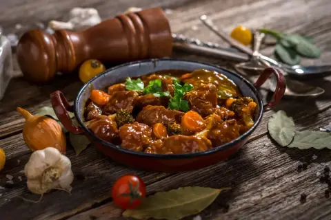 Un delicioso caldereta de cordero, con trozos tiernos de carne, zanahorias y brócoli, servido en una cazuela rústica.