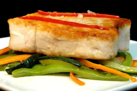 Bonito jugoso sobre verduras salteadas, con tiras de pimiento rojo.