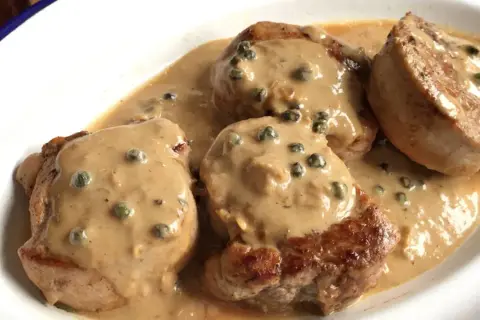 Cuatro medallones de solomillo a la pimienta, cubiertos con una cremosa salsa de pimienta verde, servidos en un plato blanco.