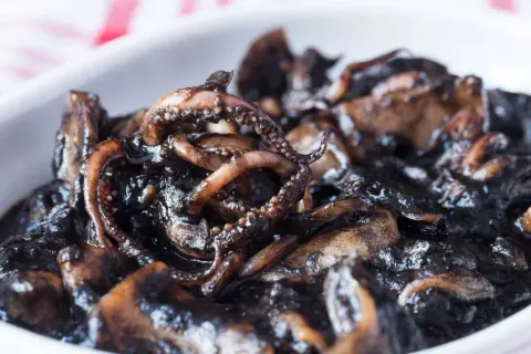 Un plato de calamares en su tinta, con tentáculos visibles y una salsa oscura y brillante.
