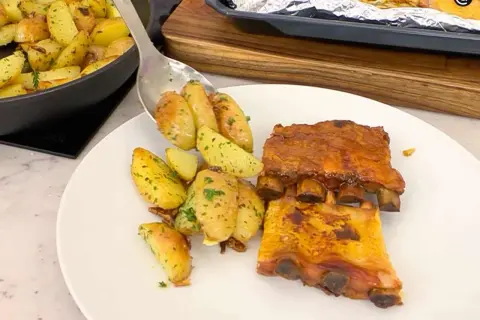 Costillas de churrasco al horno con patatas asadas y hierbas.