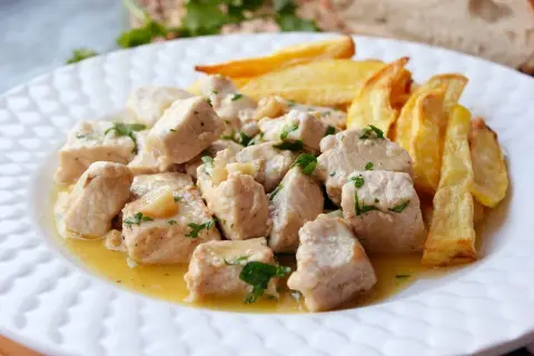 Sabroso lomo al ajillo en trozos, bañado en aceite y ajo, con patatas fritas doradas al lado.