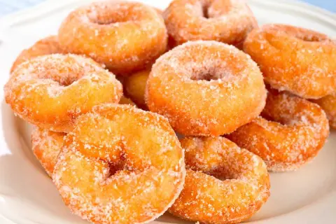 Montón de rosquillas caseras de toda la vida, doradas y espolvoreadas con azúcar, listas para disfrutar.