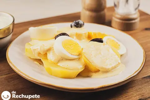 Papa a la huancaina servida en un plato blanco, con rodajas de huevo duro y aceitunas negras.