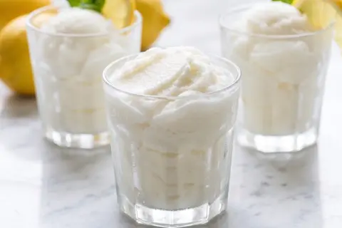 Tres vasos de sorbete de limón refrescante, con limones amarillos y hojas de menta en el fondo.
