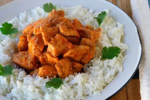 Sabroso pollo tikka masala cubierto con arroz blanco y decorado con cilantro fresco.