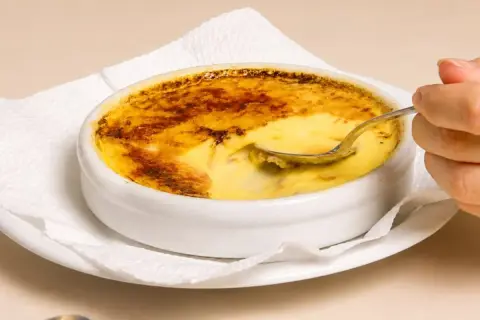 Una cuchara se hunde en un cremoso creme brulee con una capa superior caramelizada y dorada.