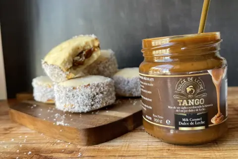Alfajores cubiertos de coco y un frasco de dulce de leche Tango, listos para disfrutar.