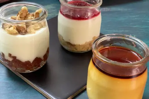 Tres postres en frascos: uno con nueces, otro con mermelada y galleta, y un flan de queso con caramelo.