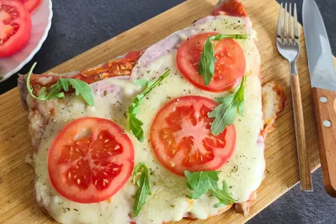 Un delicioso matambre a la pizza, cubierto de queso derretido, rodajas de tomate fresco y rúcula, servido en tabla de madera.